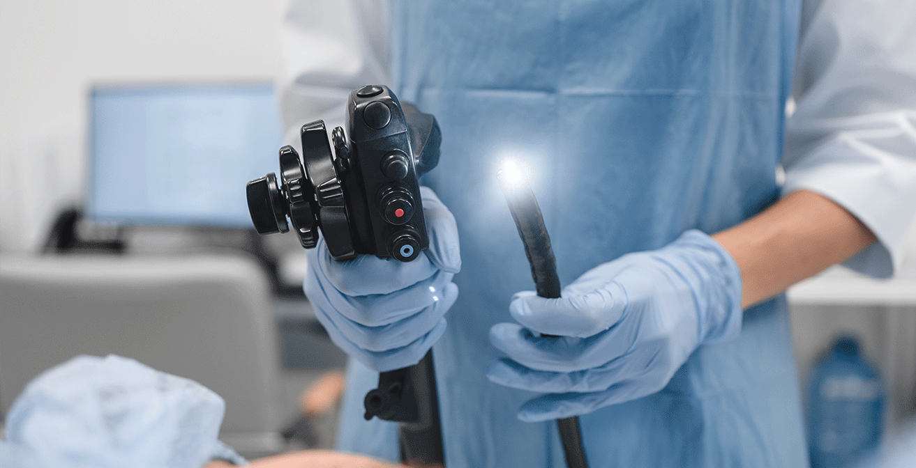 Healthcare professional wearing blue protective gloves holding a flexible fibre‑optic endoscope used for gastrointestinal examinations such as colonoscopy.