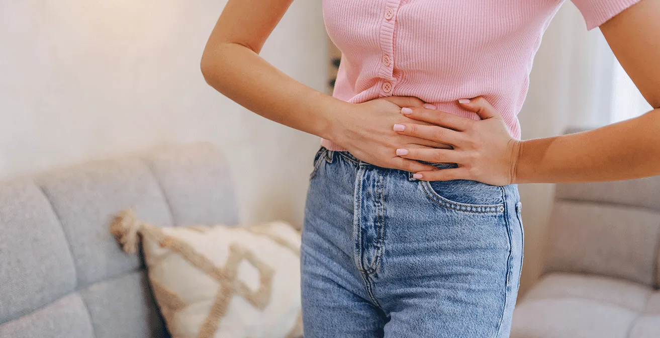 Woman holding her lower abdomen in discomfort, illustrating abdominal pain associated with inflammatory bowel disease (IBD).